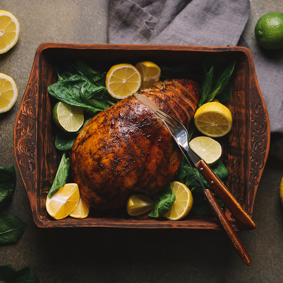 Piept de curcan feliat, cu lămâi, lime și spanac, într-o tavă de lemn.