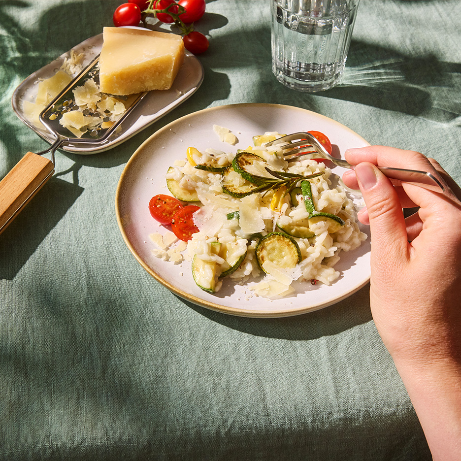 Risotto cu dovlecei și roșii cherry, cu parmezan ras, pe o față de masă verde.