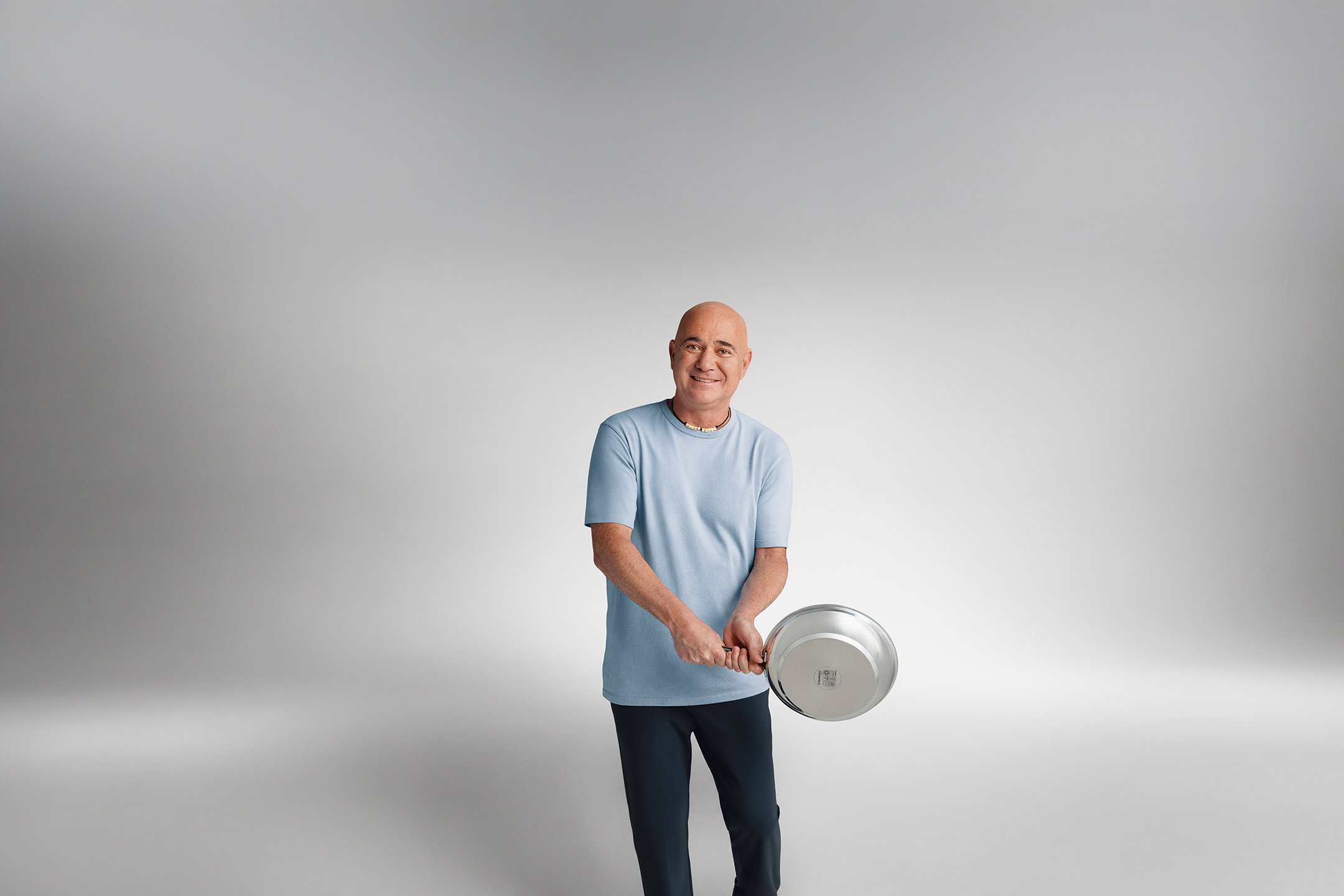 Andre Agassi într-un tricou albastru ține o tigaie în mâini.