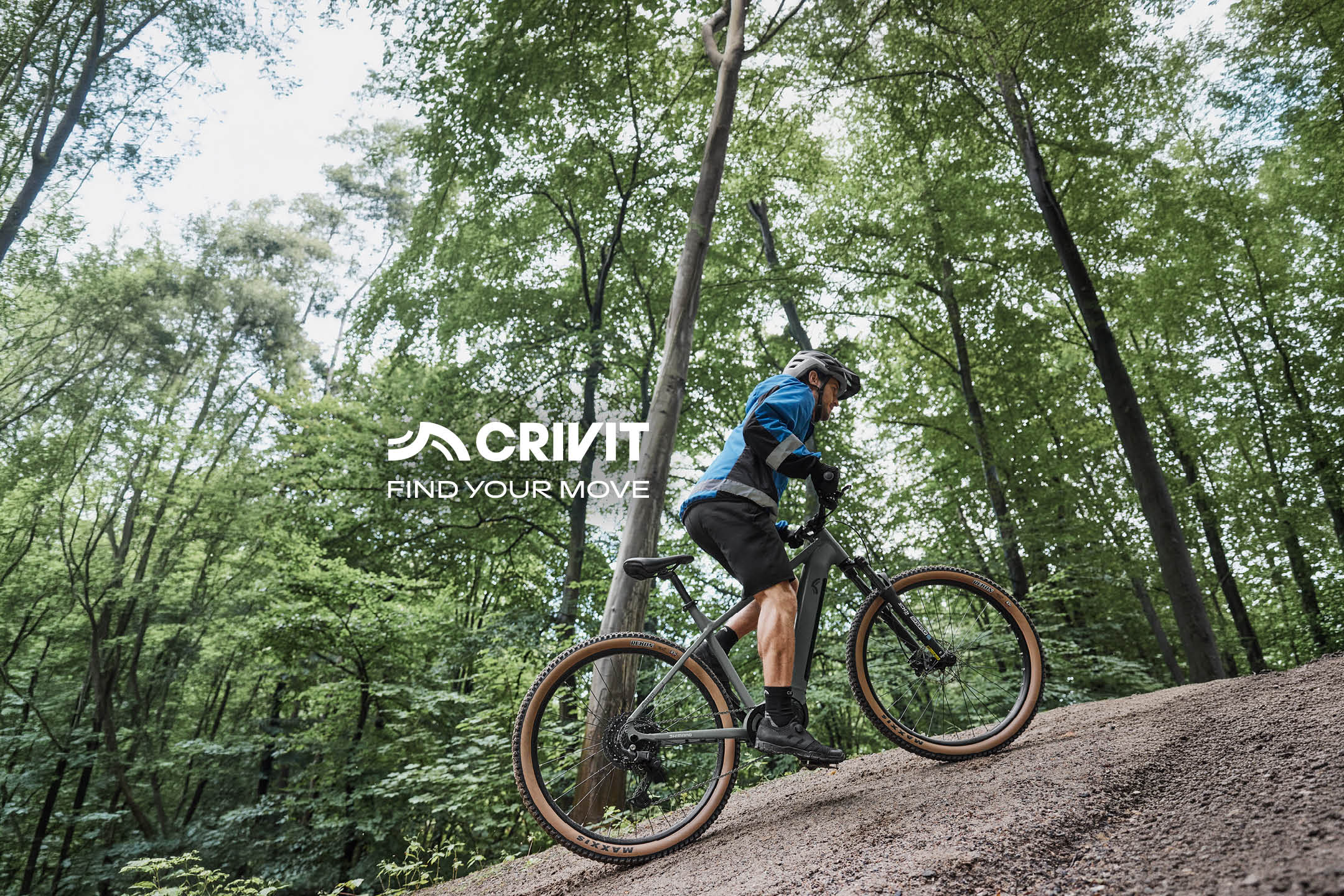 Bărbat pe bicicletă electrică de munte, urcând o pantă în pădure. Text: CRIVIT FIND YOUR MOVE.