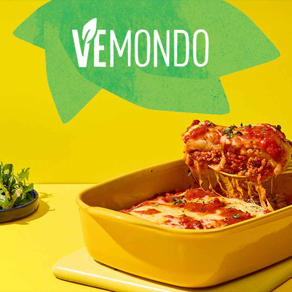 Lasagna vegană cu sos roșu și brânză topită, servită într-un vas galben, cu salată verde.