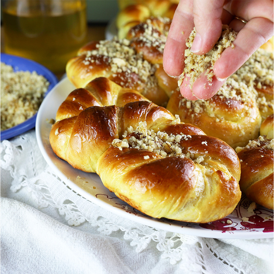 Chifle dulci împletite, glazurate și presărate cu nuci, pe o farfurie albă.