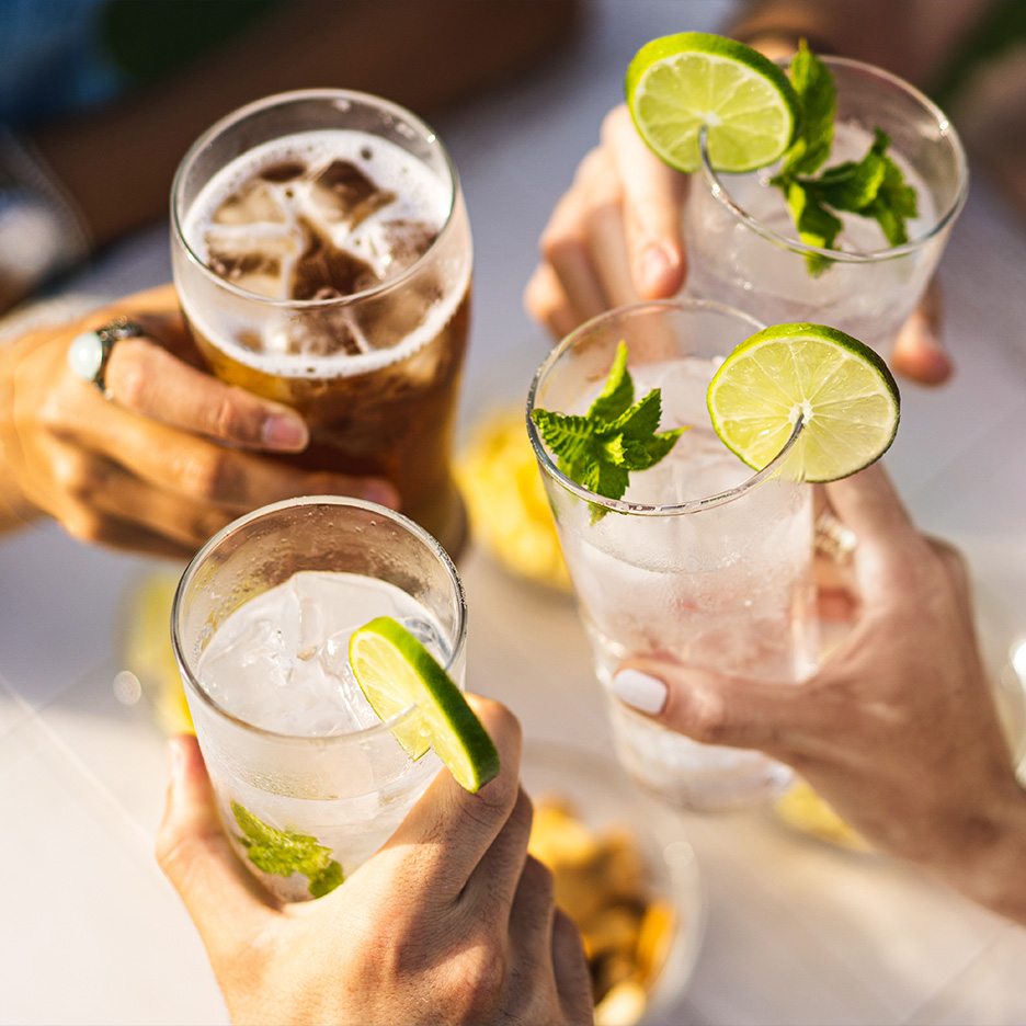 Mână care ține o bere, cocktailuri cu gheață, lămâie verde și mentă.