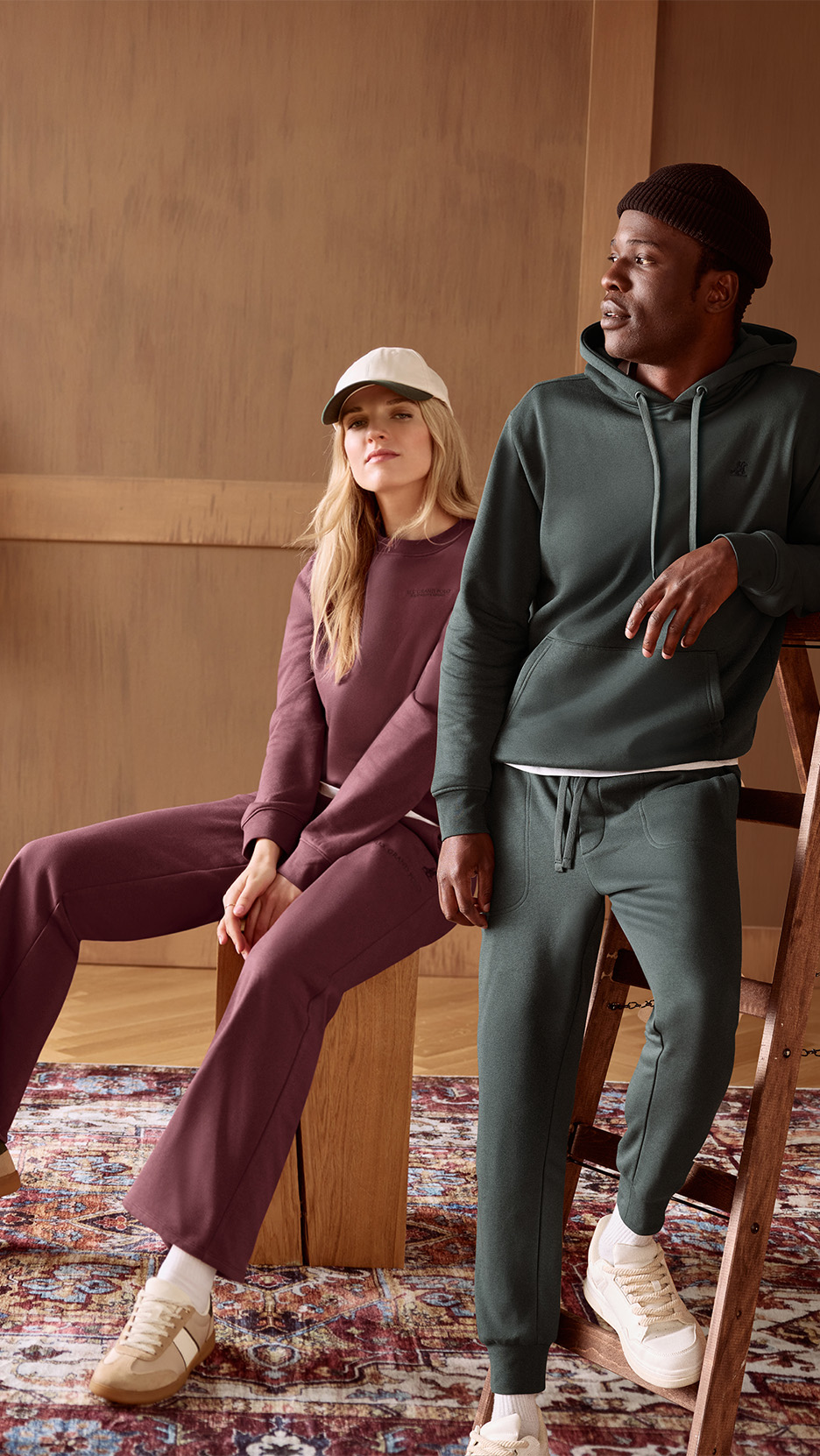 Un bărbat și o femeie poartă treninguri asortate, unul verde închis, celălalt vișiniu.