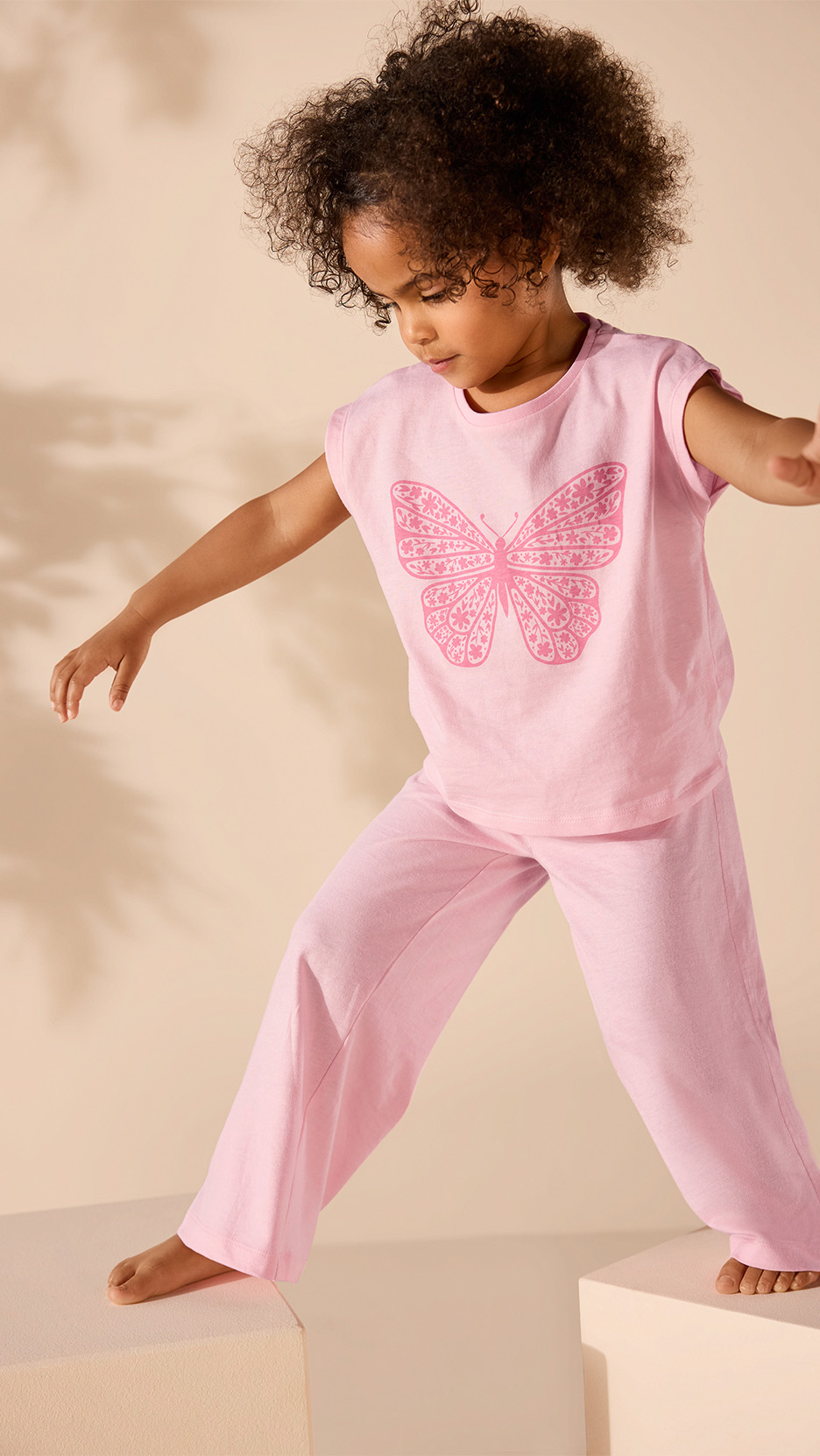 Fetiță într-un set de pijamale roz cu fluture, stând pe cuburi.