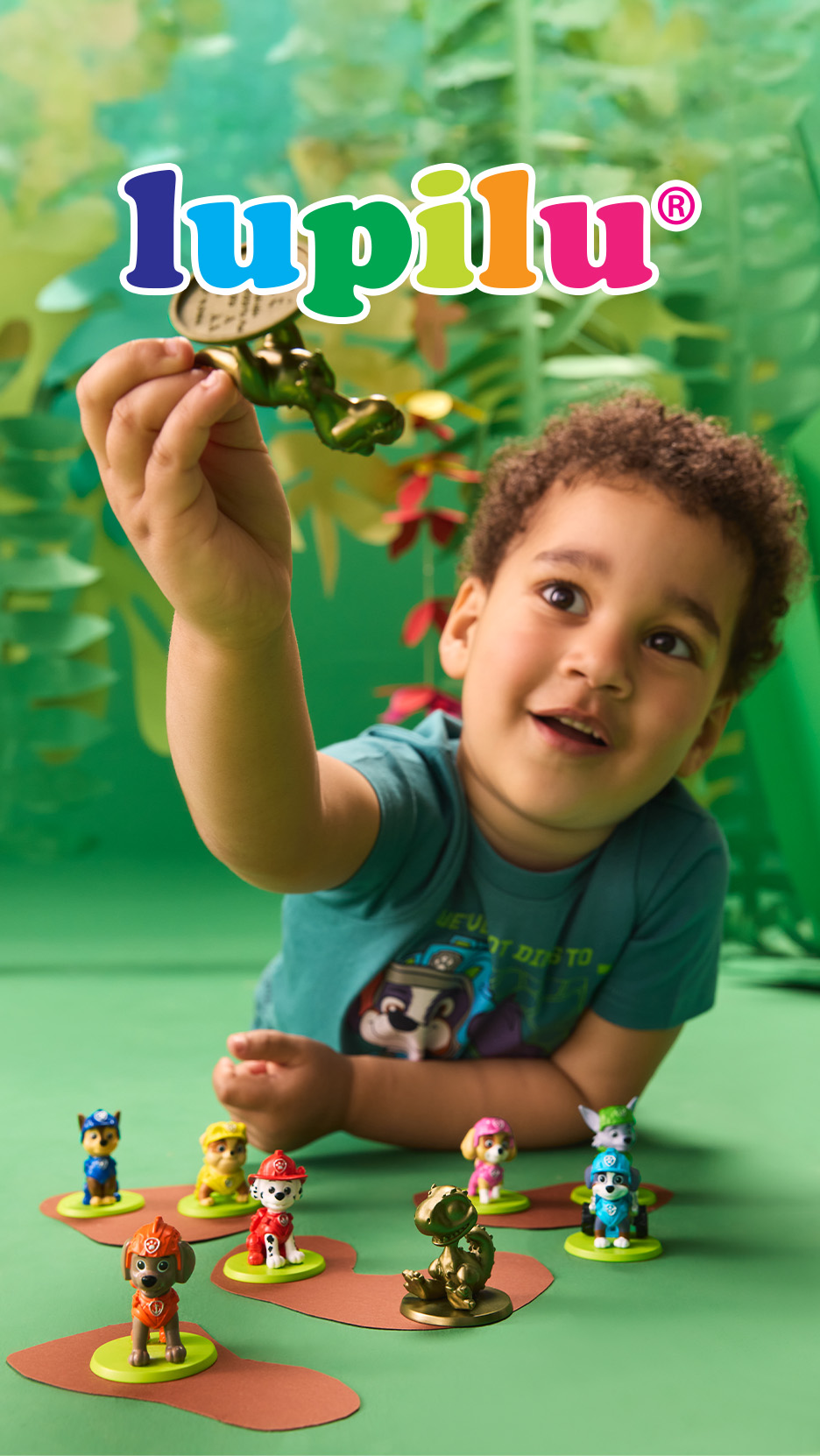 Un copil se joacă cu figurine de căței și un dinozaur auriu, pe un fundal verde cu frunze.
