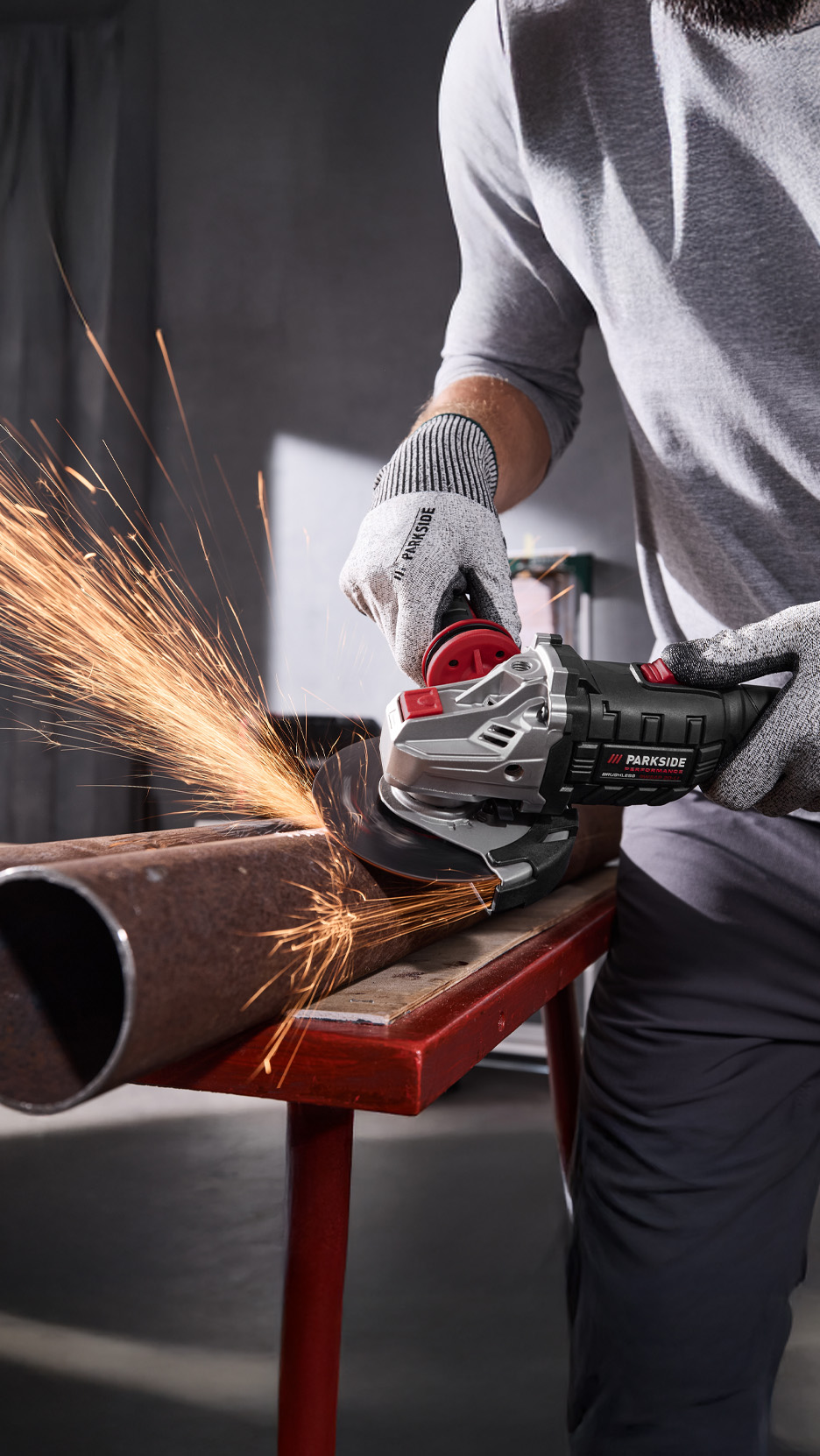 Un bărbat folosește un polizor unghiular Parkside pentru a tăia o țeavă metalică, generând scântei.