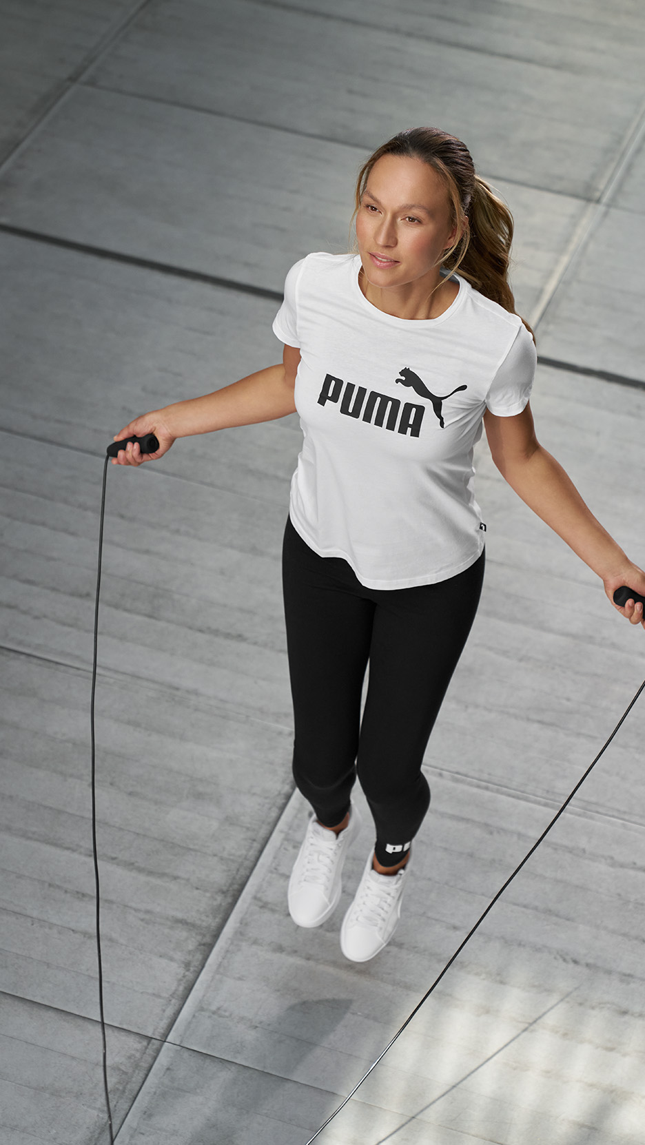 Femeie în tricou alb și colanți negri, sărind coarda.
