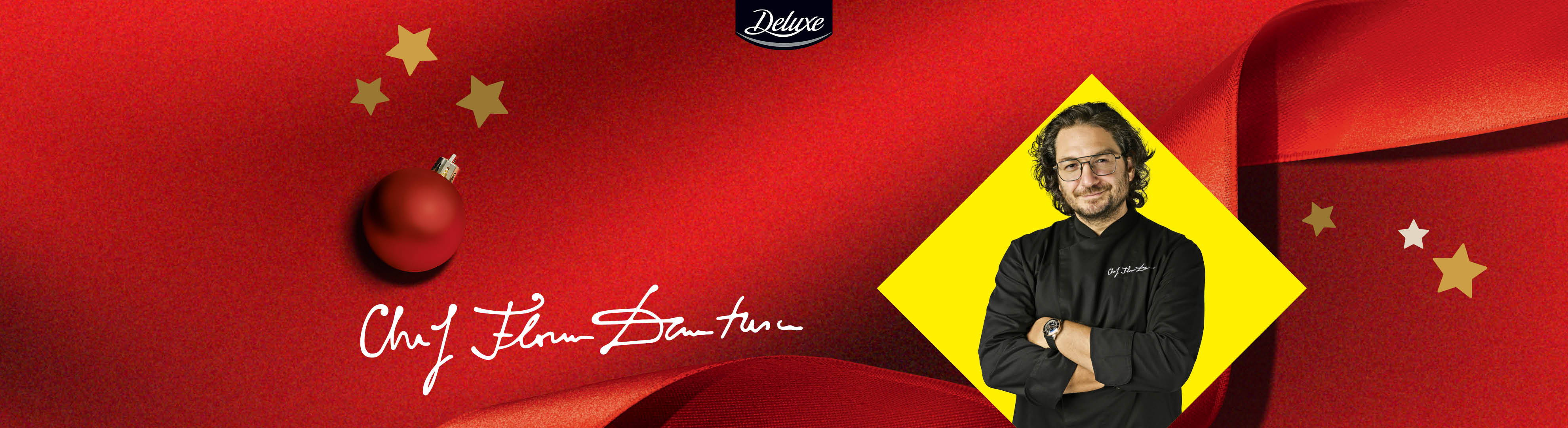 Un chef zâmbitor, o decorațiune roșie de Crăciun și stele aurii pe un fundal roșu, cu logo-ul Deluxe.