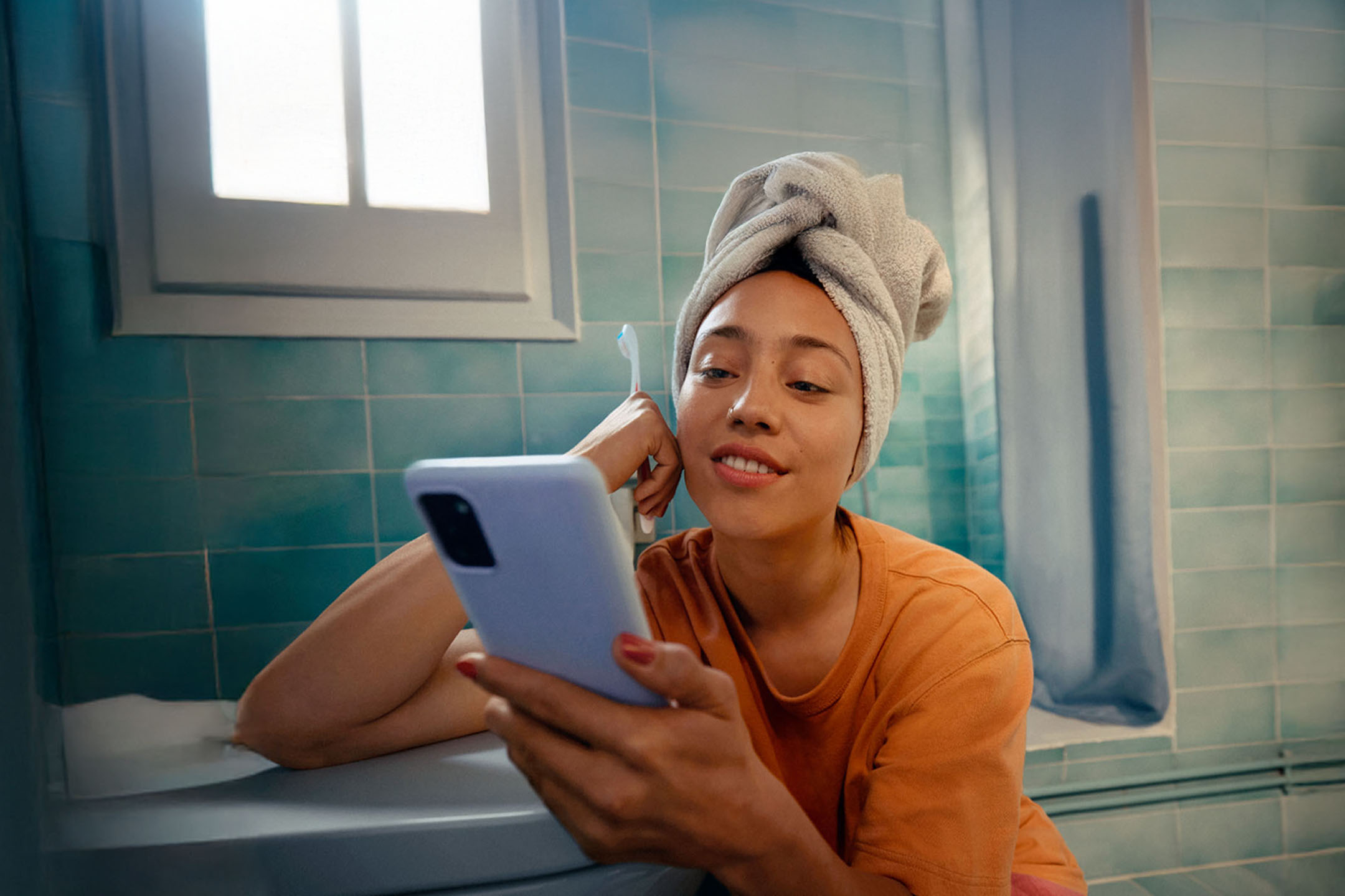 Femeie cu prosop pe cap, folosind un smartphone în baie.