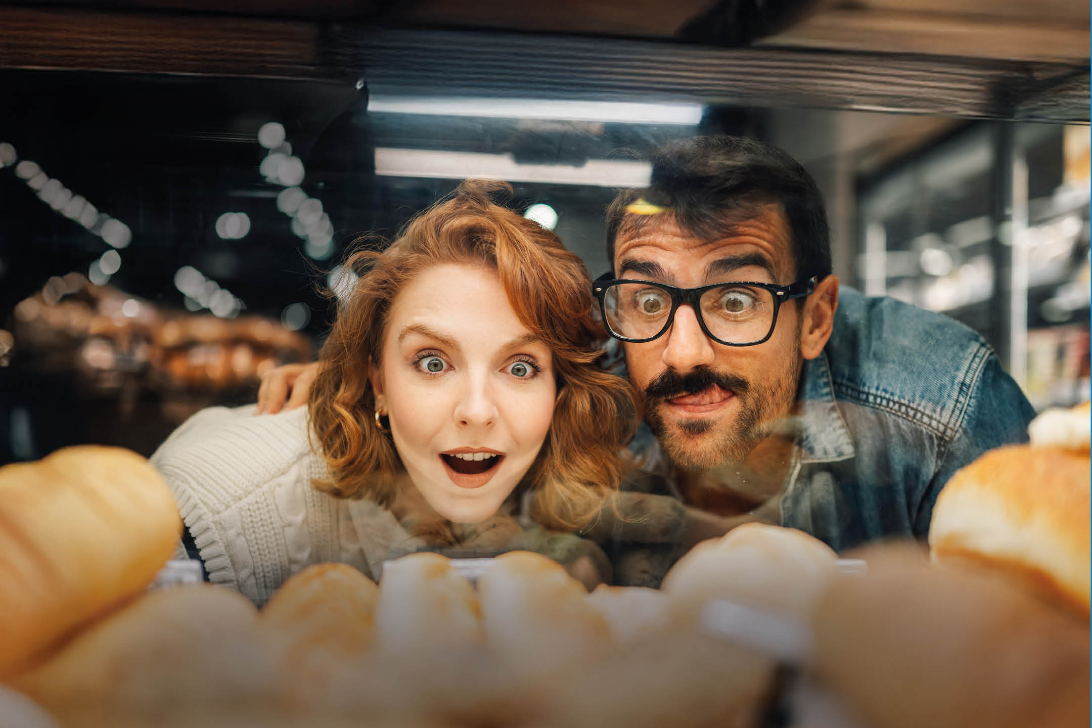 Doi oameni uimiți privesc la produse de patiserie într-o vitrină.