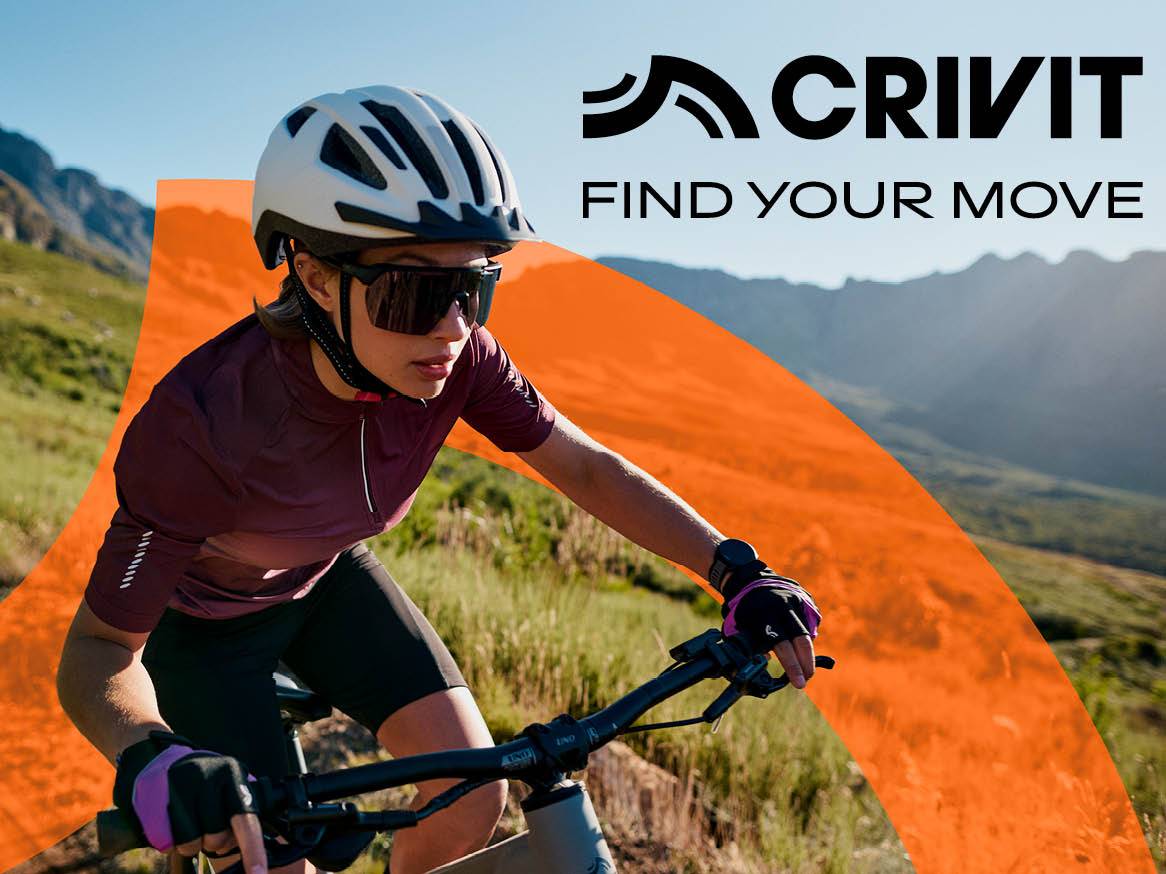 O femeie poartă o cască și ochelari de soare în timp ce merge pe bicicletă pe un drum de munte.