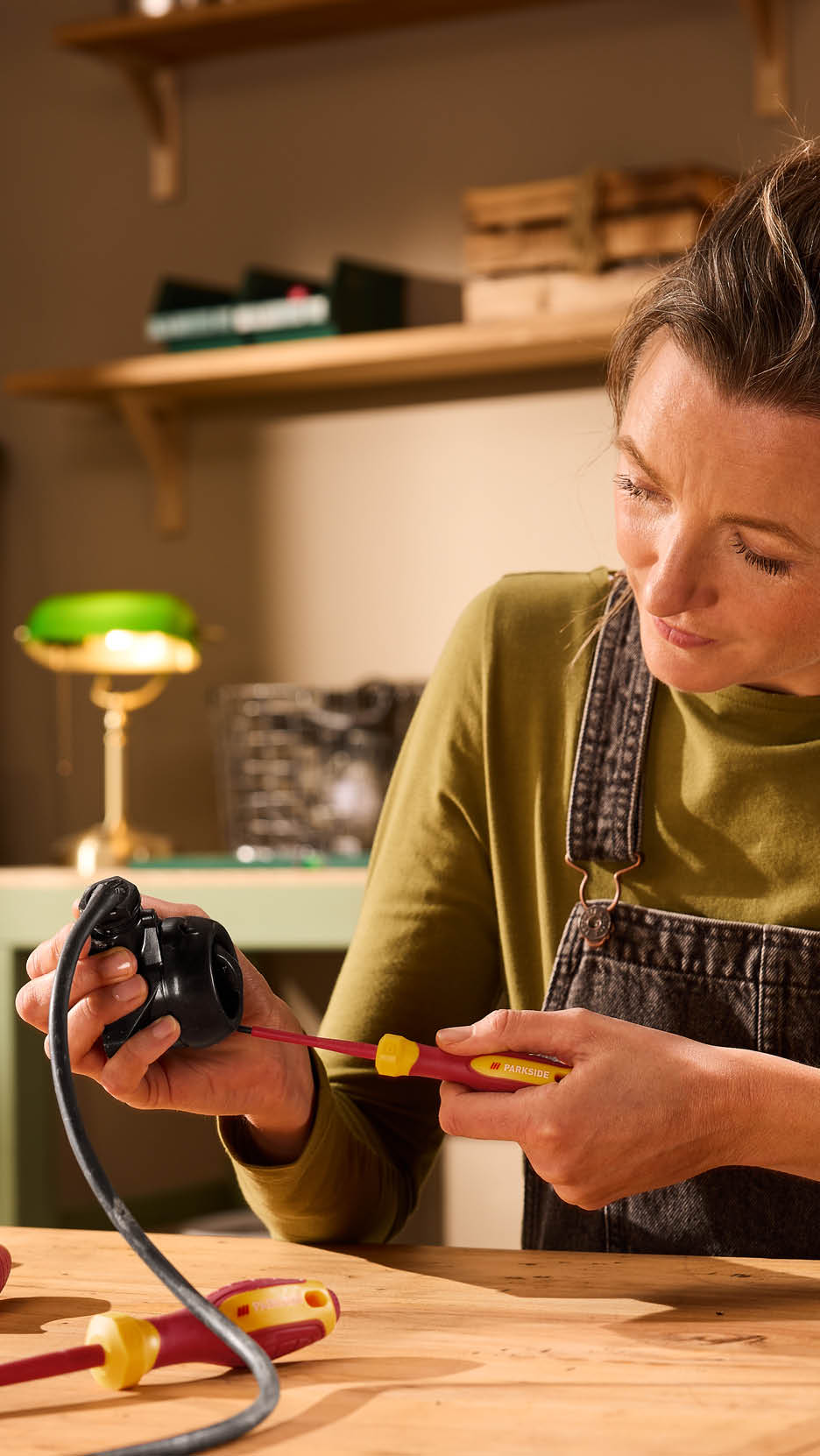 Femeie reparând un cablu electric cu o șurubelniță, pe o masă de lemn.