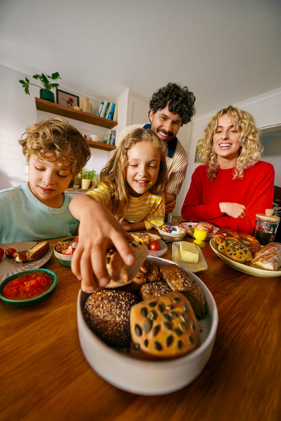 Familie zâmbitoare la masă, cu pâine proaspătă, iaurt cu fructe și unt.